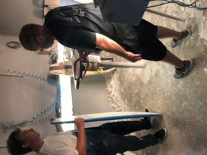 Two men standing in a room with a surfboard and Supreme