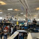 A group of people standing around a Supreme boat in a warehouse.
