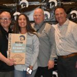 Four people posing with a plaque in front of a Supreme Boats wall.