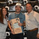 Three people admiring a Supreme Boats plaque displayed on a wall.