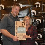A couple holding a Supreme Boats plaque in front of a wall.