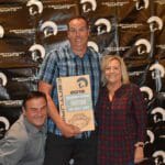 Three people posing with a Supreme Boats plaque in front of a wall.