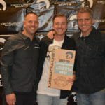 Three men standing in front of a Supreme Boats banner with an award.