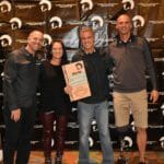 Four people posing for a picture in front of a Supreme banner.