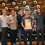 A group of men posing for a picture in front of a Supreme banner.