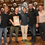 A group of people posing in front of a Supreme Boats banner.