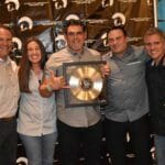 A group of people posing for a picture with a gold record from Supreme Boats.