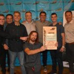 A group of men posing in front of a Supreme banner.