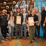 A group of people posing for a picture in front of a Supreme banner.