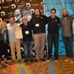 A group of people posing in front of a Supreme banner.