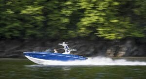 Blue 2023 Supreme cruising down lake with greenery behind it.