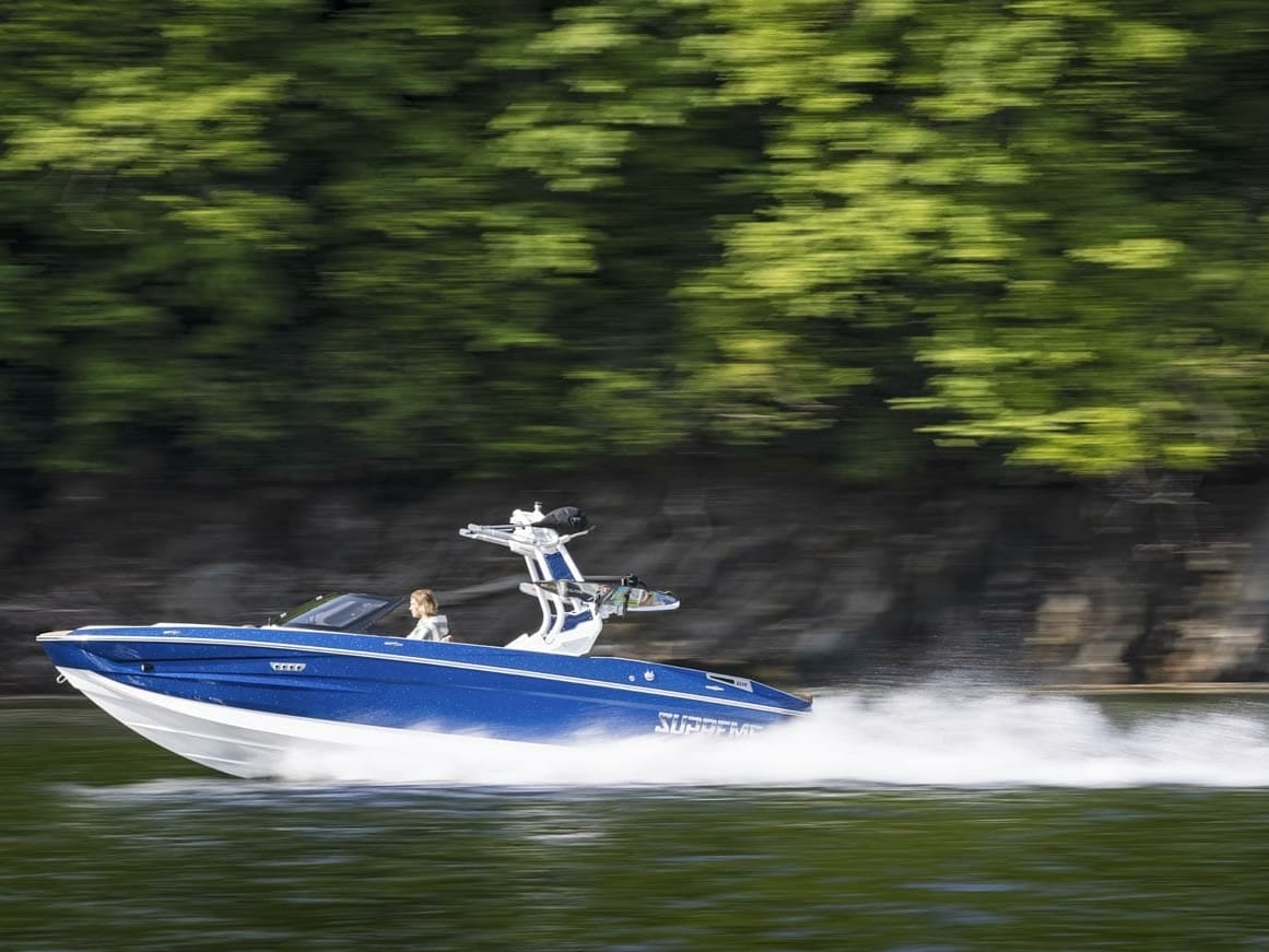 Blue 2023 Supreme cruising down lake with greenery behind it.