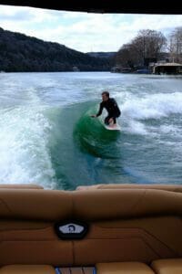 A man riding a surfboard on a Supreme boat.