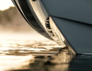 Close-up view of a Supreme boat's bow cutting through calm water at sunrise or sunset, with reflections and mist visible on the surface.