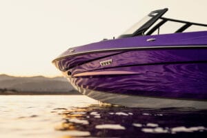 Close-up of the front side of a 2026 Supreme S220 purple speedboat on calm water at sunset, with distant mountains in the background.