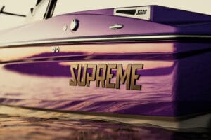 Close-up of the side of a purple 2026 Supreme Towboats S220 with sunlight reflecting on the water and hull.