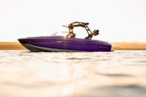 A Supreme 2026 S220 speedboat floats on calm water at sunset, with hills visible in the background.