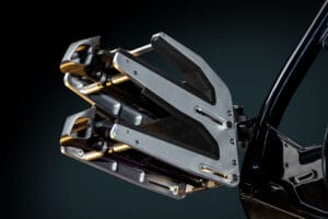 A close-up view of a metallic robotic gripper with padded inner surfaces, mounted on a black arm—reminiscent of the sleek engineering found in the Supreme S220—set against a dark background.