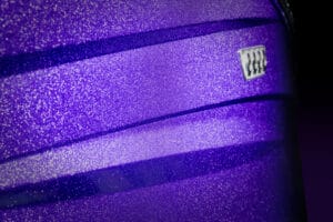 Close-up of a metallic purple 2026 Supreme Towboats S220 surface with a subtle ridged design and a small rectangular silver badge featuring four black dots.