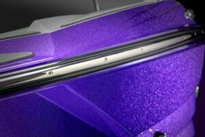 Close-up of a Supreme S220 purple metallic boat hull with chrome trim and a sparkling texture, photographed under bright light.