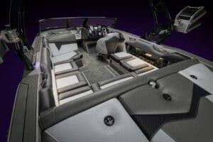 The interior of the Supreme Towboats S220 luxury speedboat features gray and black cushioned seating, a sleek steering console with controls, and accent lighting that stands out against the dark background.