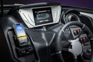 A 2026 Supreme dashboard with a digital display, smartphone mounted on the left, various buttons, and a Supreme S220 steering wheel in the foreground.