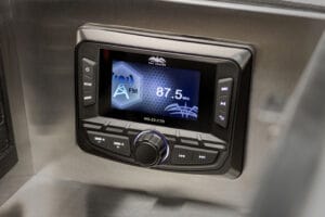 Close-up of a digital radio tuner display set to 87.5 MHz FM, with various control buttons and a central knob below the screen—inside the premium cockpit of a Supreme S220.