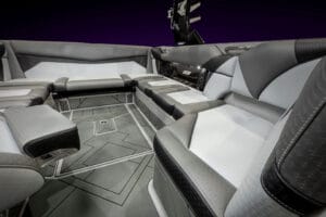 Luxury boat interior of the 2026 Supreme S220 featuring geometric patterned flooring, cushioned gray and white seating, and built-in speakers, all illuminated under soft lighting.