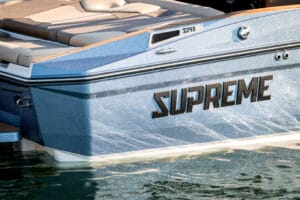 Close-up of the rear side of a blue 2026 Supreme Boats S240 partially in the water, showcasing seating and boat details.