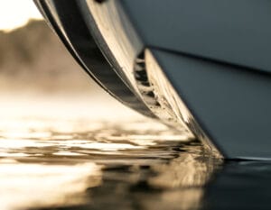 Close-up view of the 2026 Supreme Boats S240’s hull cutting through calm water, with sunlight reflecting off the surface and creating a serene, golden glow.