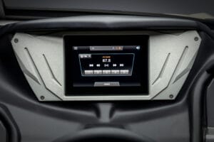 Close-up of a car dashboard touchscreen displaying an FM radio station set to 87.5, with playback and zone control buttons visible—perfect for tuning in while cruising in your Supreme Boats S240.