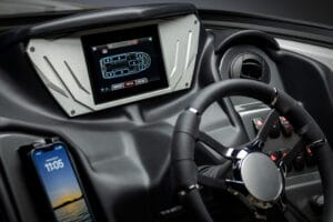 A close-up of a Supreme S240 boat’s dashboard showing a digital touchscreen display, a steering wheel, several control buttons, and a smartphone mounted to the side displaying the time.