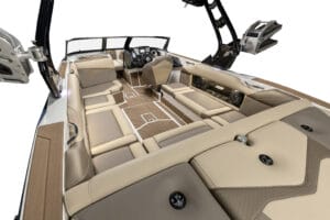 Interior view of a Supreme S240 motorboat featuring beige and tan cushioned seating, control panel, and wakeboard tower against a white background.