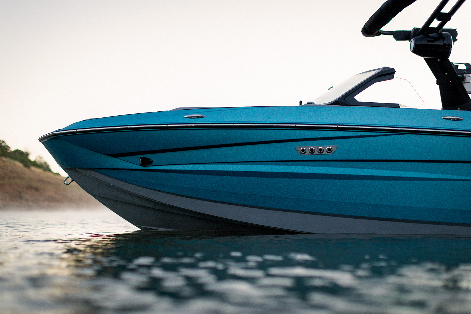 Close-up of the side and front deck of a blue Supreme S240 motorboat on calm water, with a hillside visible in the background under a clear sky.
