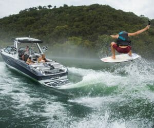 A man is wakeboarding behind a Supreme boat.
