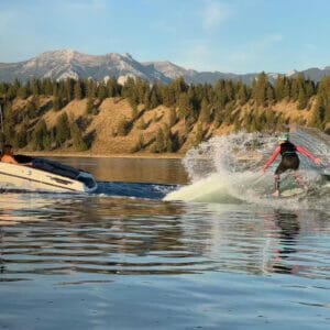A person is riding a surfboard near a Supreme boat in the water.