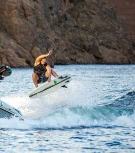 A man is wakeboarding behind a Supreme boat.