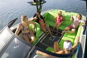 A group of five people sit and relax on the bright green seats of a Supreme Towboats S220, enjoying a sunny day on the water.