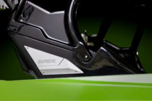 Close-up of a lime green and black vehicle part with a silver panel. The panel has the word "Supreme" inscribed on it, set against a green and black gradient background. This detail is from the impressive Supreme S220 model.