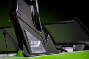 Close-up view of a section of a lime green and black Supreme S220 towboat, featuring a "Supreme" logo on a metallic plate. The background is blurred and dark.