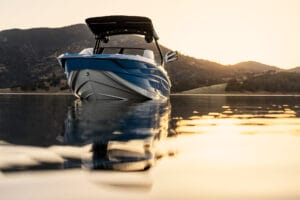 A Supreme S240 boat in blue and white floats on calm water at sunset, with mountains in the background.