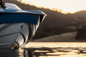Close-up of the Supreme S240's bow on calm water at sunset, with hills and trees in the background.