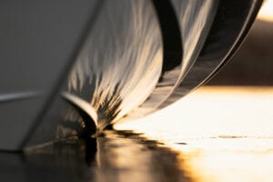 Close-up view of a Supreme Boats S240 hull reflecting in calm water during sunset, showing intricate reflections on the water surface.