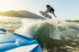 A person is performing an airborne maneuver on a wakeboard, soaring above a wave created by the Supreme S240 in a body of water with a mountainous landscape in the background.
