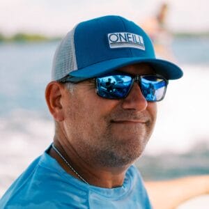 Wally, a man wearing sunglasses and a hat, is on a boat.