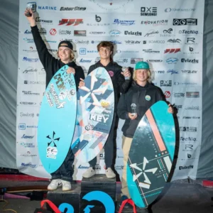 Three surfer athletes, including Cade and Lybeck, proudly standing on top of a podium with their surfboards.
