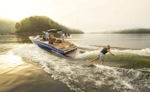 A person wake surfing behind a Supreme Wakeboats vessel on a misty lake, with another person driving the boat and two passengers watching.