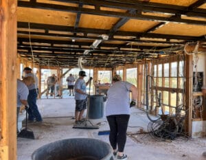 A group of people wearing casual clothes work on constructing a building's interior with exposed wooden beams, wiring, and tools scattered around, all while embodying the spirit of The Supreme Life.