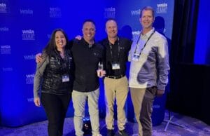 Four people pose in front of a blue backdrop adorned with "WSLA Summit" logos, dressed in casual business attire, as the dim lighting highlights the moment. Among them is the Western Sales Manager, proudly acknowledged for their recent WSIA Leadership Award.