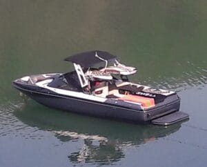 A black and white motorboat with a canopy floats on calm water. A bright orange item is on board.